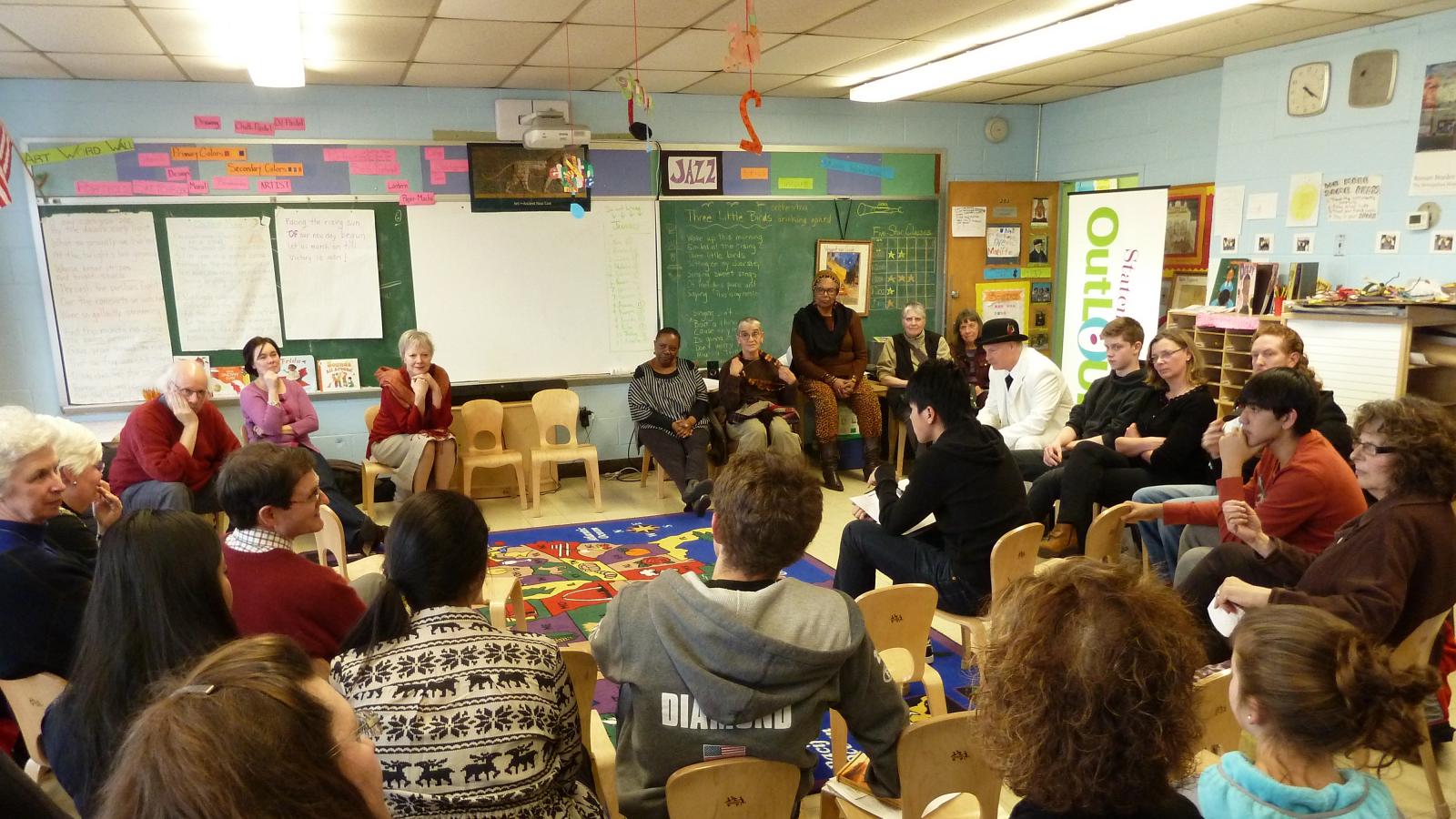 A group of people of diverse ages sit around a classroom discussing a book.