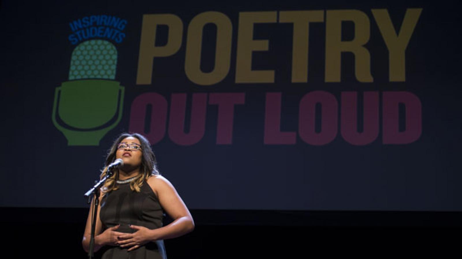 A teenage girl in a black dress speaks at a microphone with a Poetry Out Loud sign behind her.