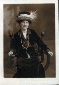 Woman wearing enormous hat sitting in chair. 