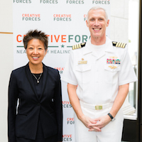  A man in military clothing is standing next to a woman smiling and posing for a picture in front of a Creative Forces sign.