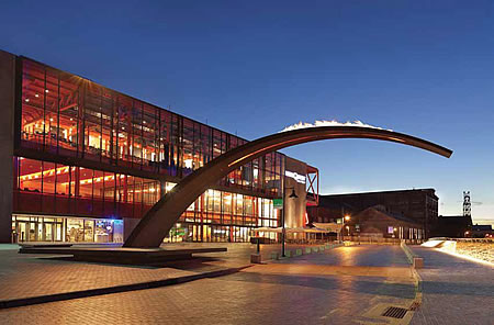 Night photo of a steel arch extending directly out from the side of a large factory building