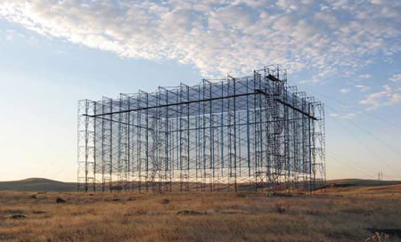 Large steel beam box-like structure in an open, fairly flat and scrubby landscape