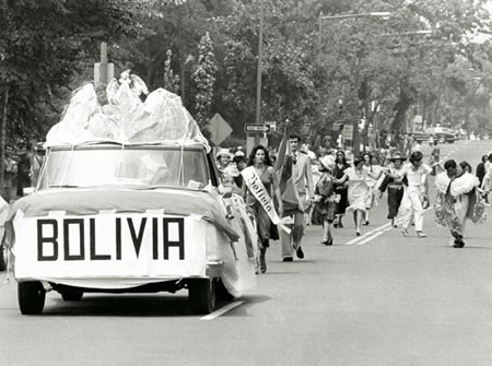 Car with the word Bolivia on a banner across the front bumper with marchers behind