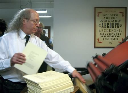 man at letterpress machine with a stack of broadsides in front of him? 