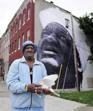 Man holding bird in front of a building with a large mural of a man's face