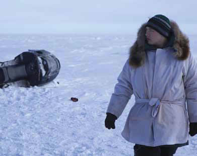 Actor in heavy winter coat in the flat arctic landscape.