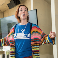  A woman stands beside a podium gesturing to the audience.
