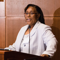  A woman stands behind a podium at the front of the room speaking. 