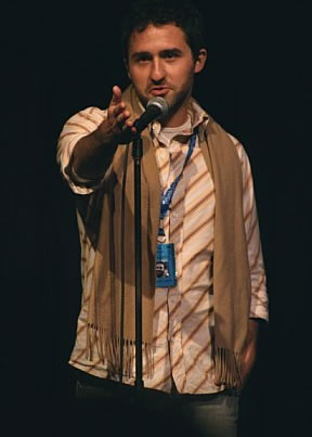 Man wearing brown scarf standing in front of microphone.