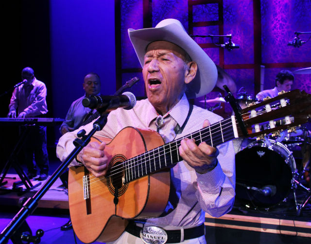 Man with cowboy hat plays guitar in front of microphone