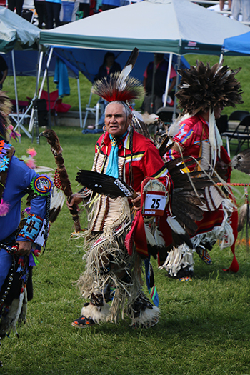 A man wearing traditional Northern Arapaho powwow wear walks across a field