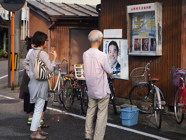 Men and women stand outside looking at a case filled with photos and a map