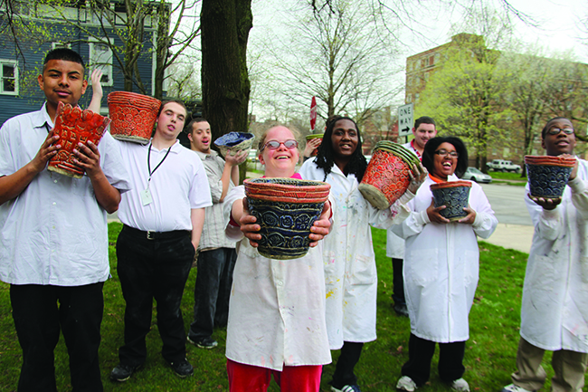 Young people with disabilities wearing painters' smocks hold out painted pieces of pottery that they created