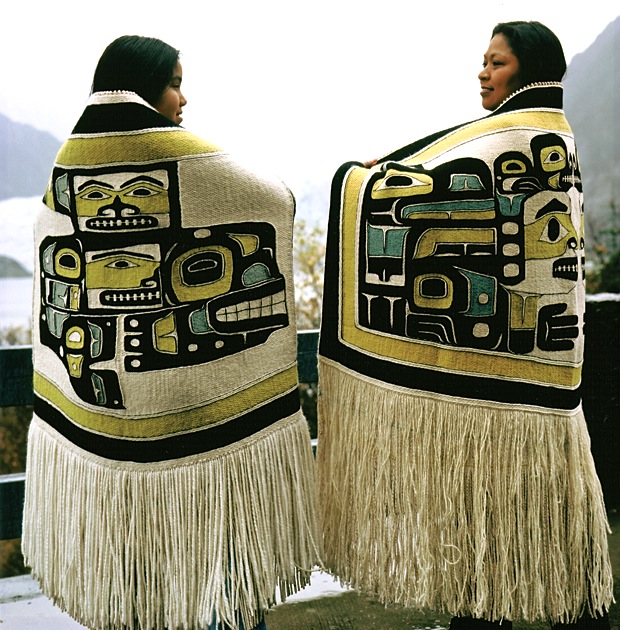 Two women draped with mantels bearing iconic stylized bird images.