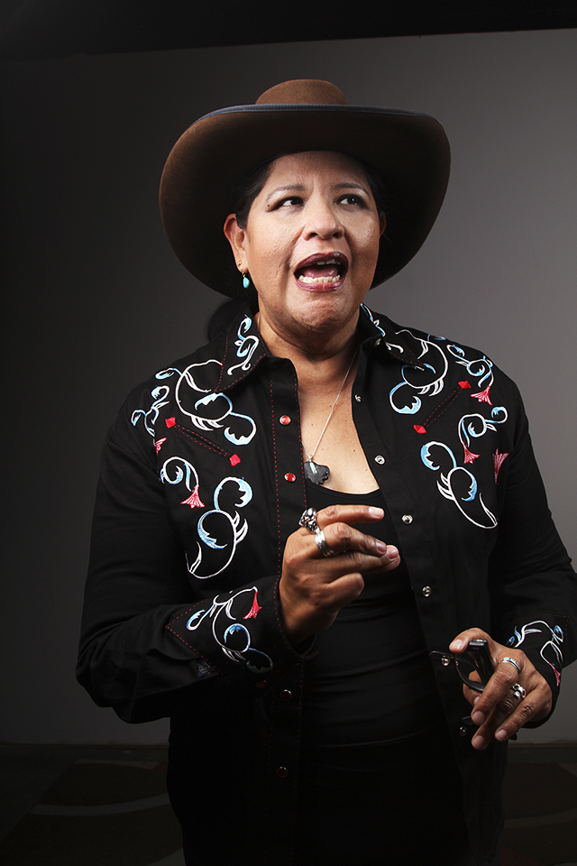 Arigon Starr Woman wearing cowboy hat, Western shirt, and holding glasses