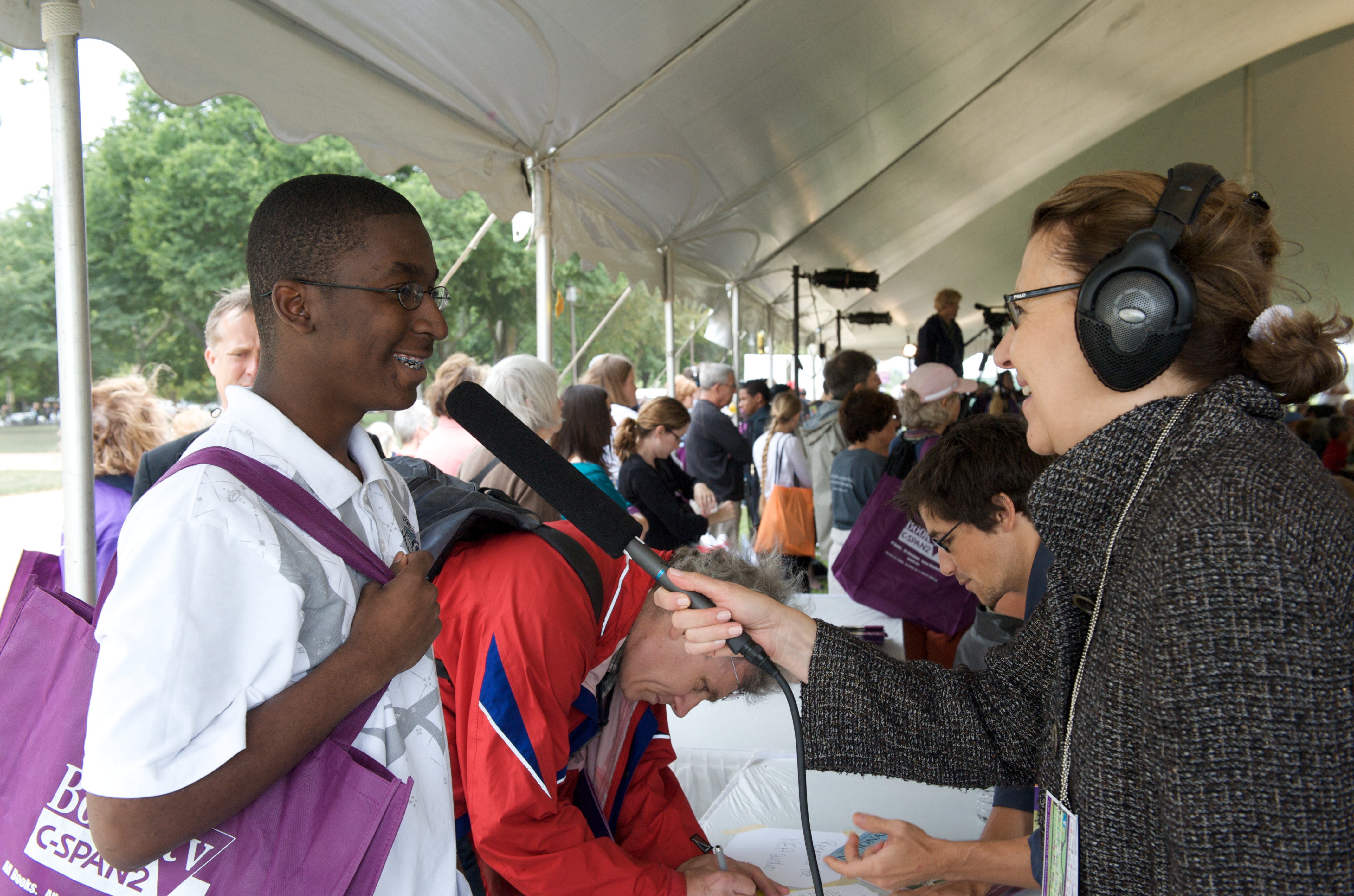 Jo Reed holding a microphone to a young visitor and asking him questions.