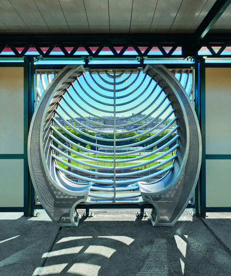 A metallic silver sculpture that resembles a peacock feather installed in front of a window