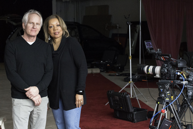 an older white man and black woman stand together on a film set