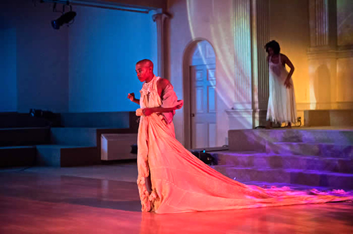 An actress stands center stage wearing a long gown.