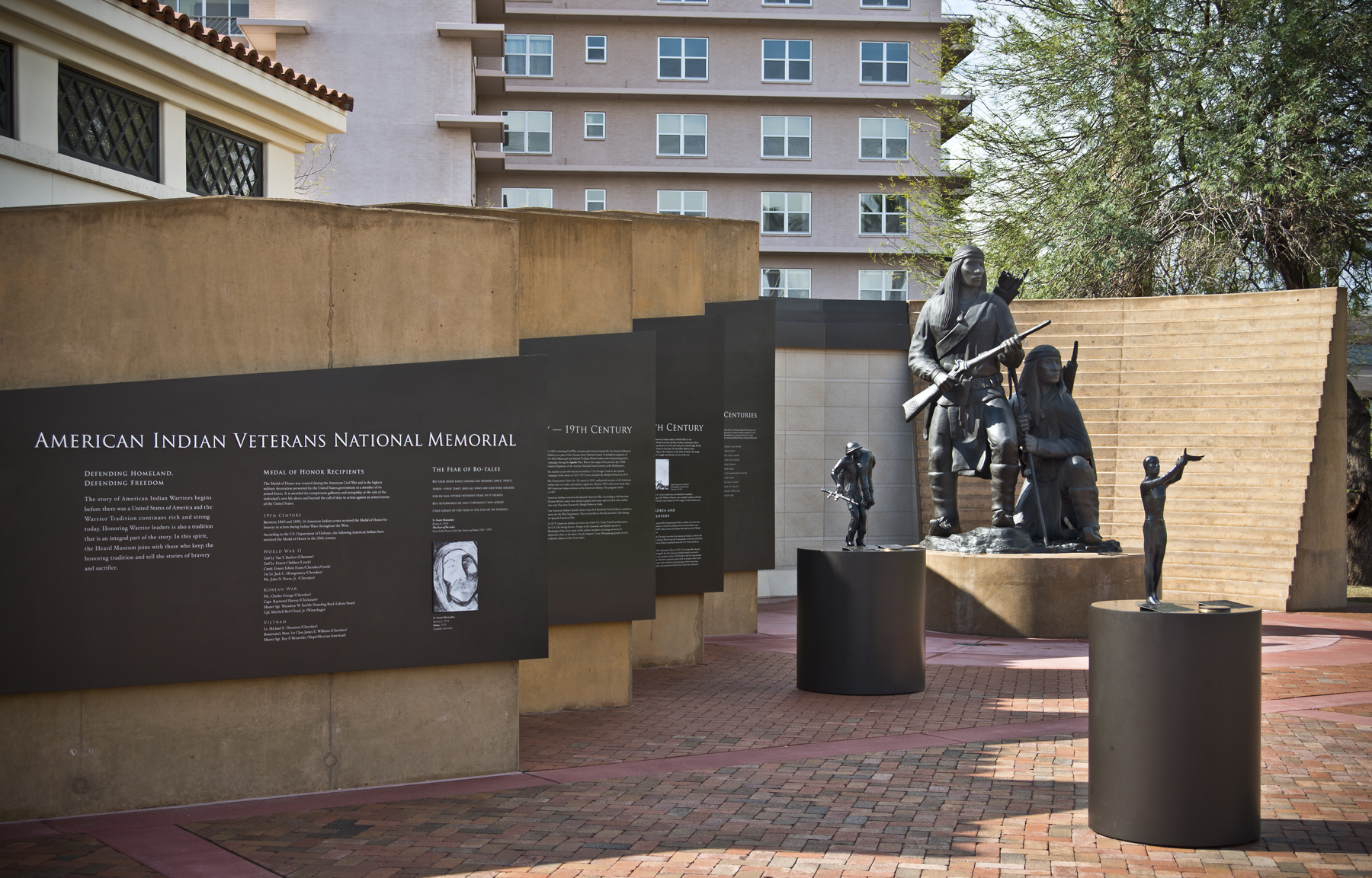 Two Native American statues standing, surrounded by walls with engraving. 