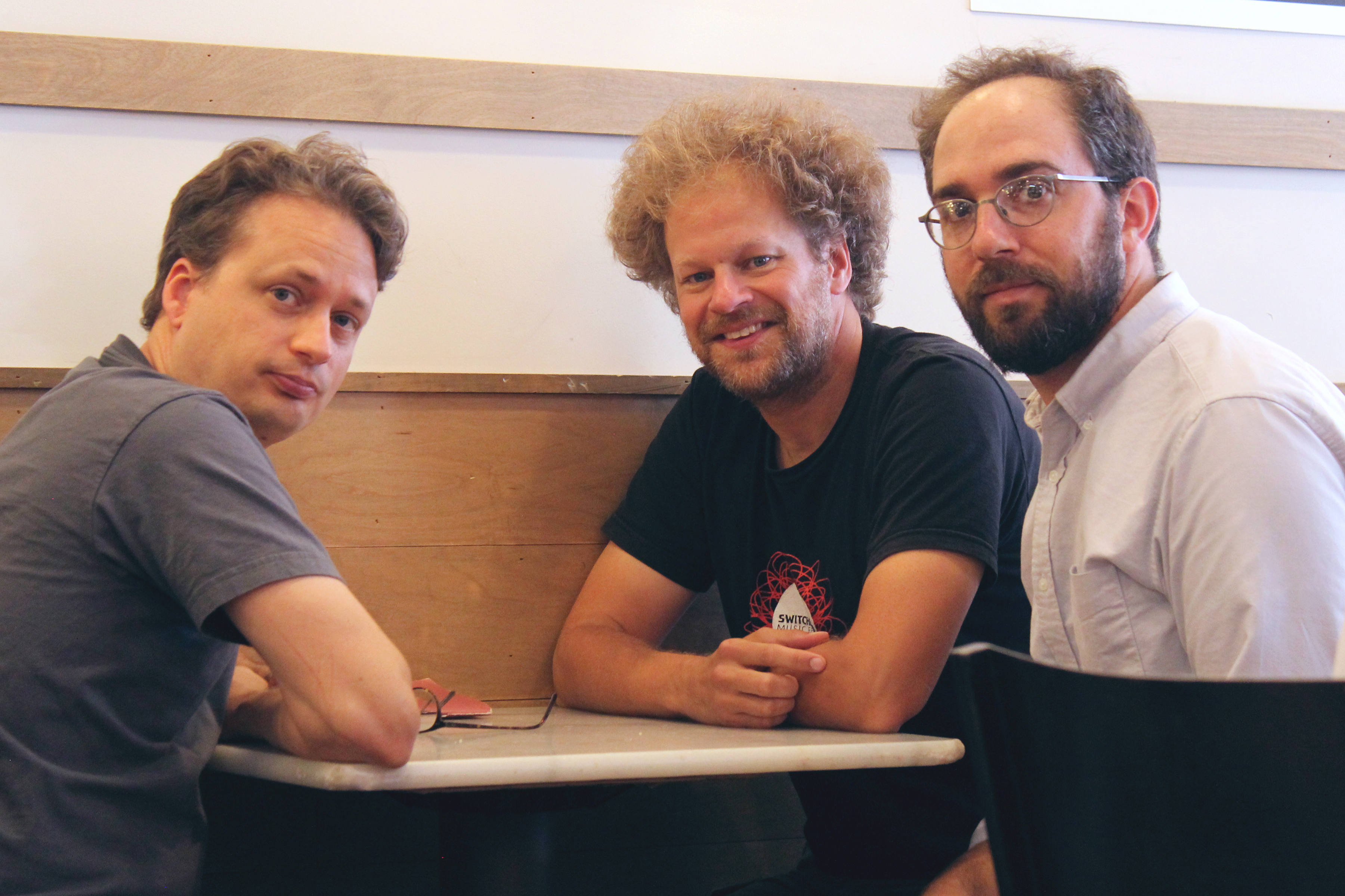 Three men sitting at a table looking at camera