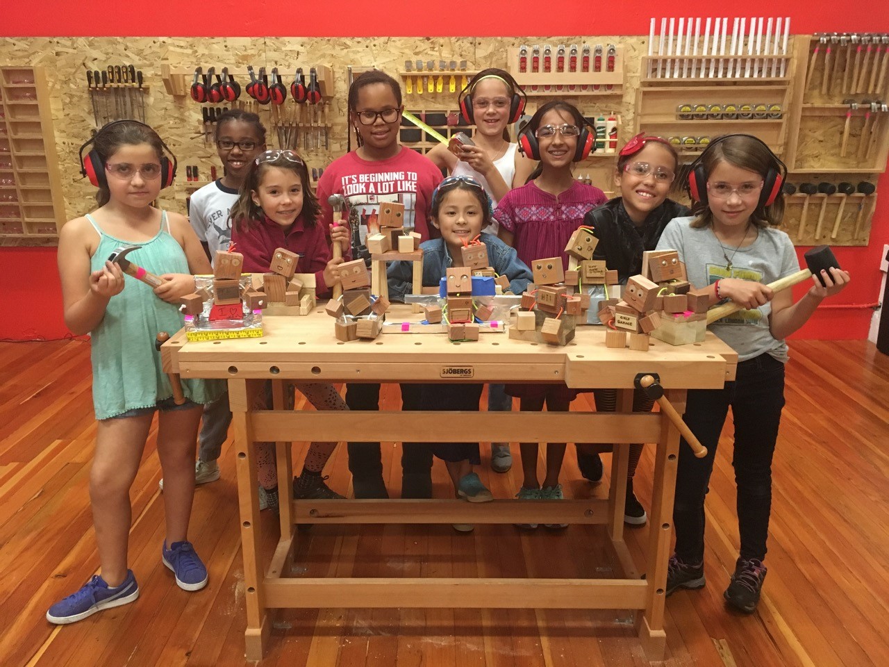 A group of girls standing around a table filled with wooden robots that they made. 