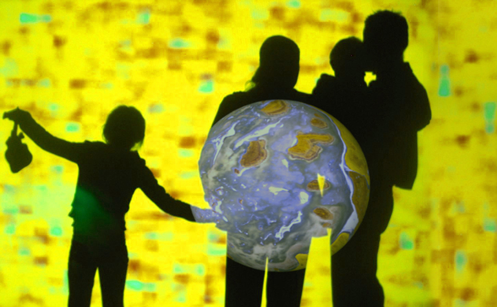 Four people in shadows in front of a bright yellow light, with an image of a planet reflected on them. 