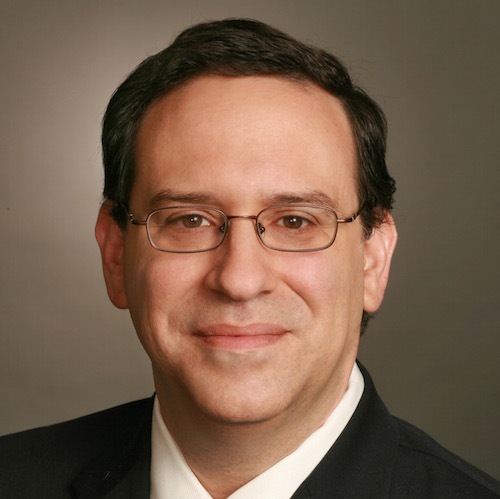 a close-up of a white man with dark hair and glasses 