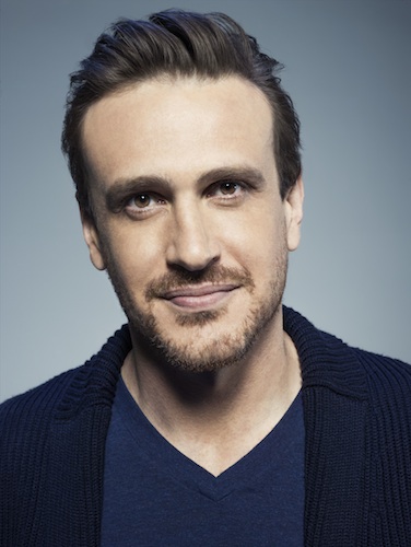 a white man with brown hair and brown eyes in blue v-neck sweater and black sportscoat
