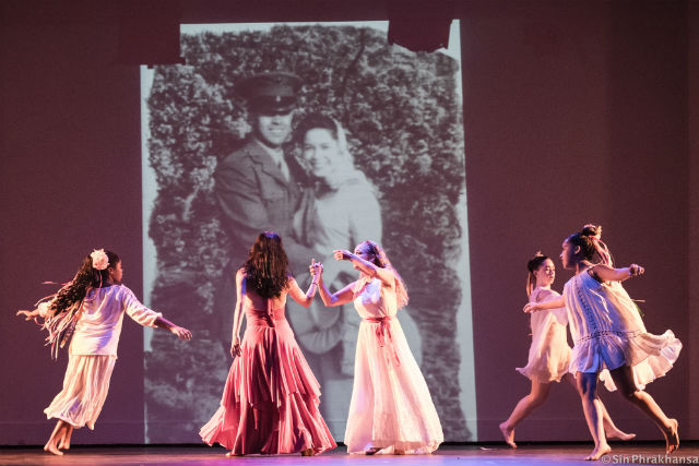 Adults and children dance on a stage in front of a giant vintage photo of a newly married couple