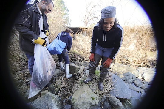 Lisa Hoffman with two other people loading trash into bags alongside shallow waterway