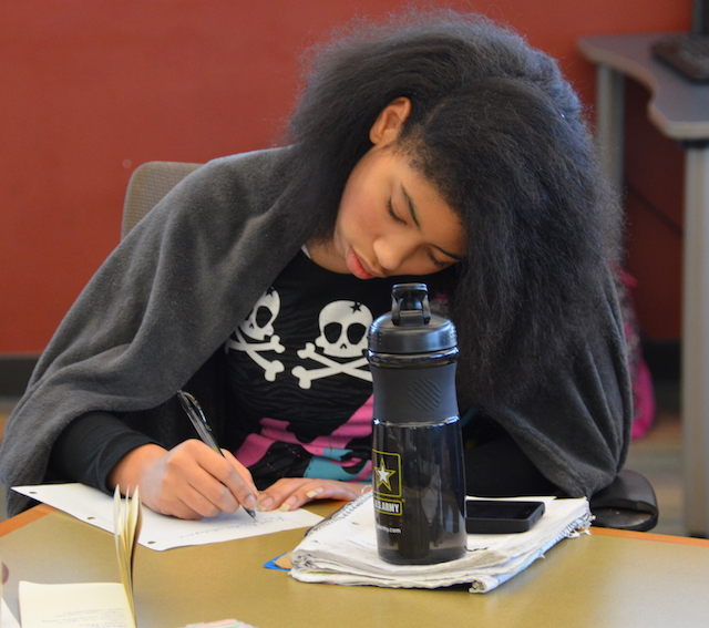 a young woman sits at a table writing in a notebook