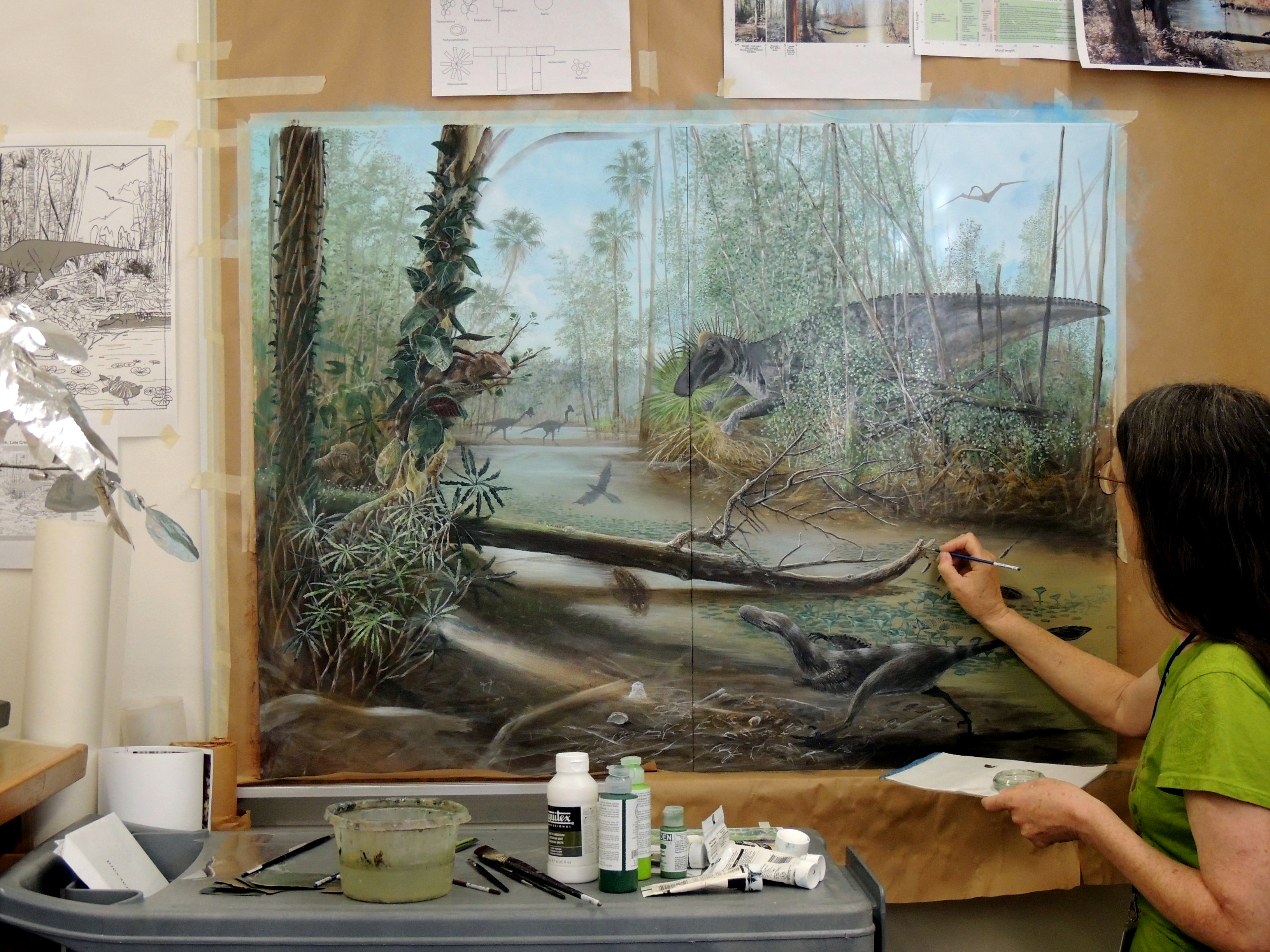 Woman painting a large highly detailed painting of dinosaurs