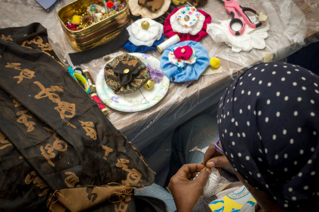A woman sews at a sewing table covered in sewing supplies