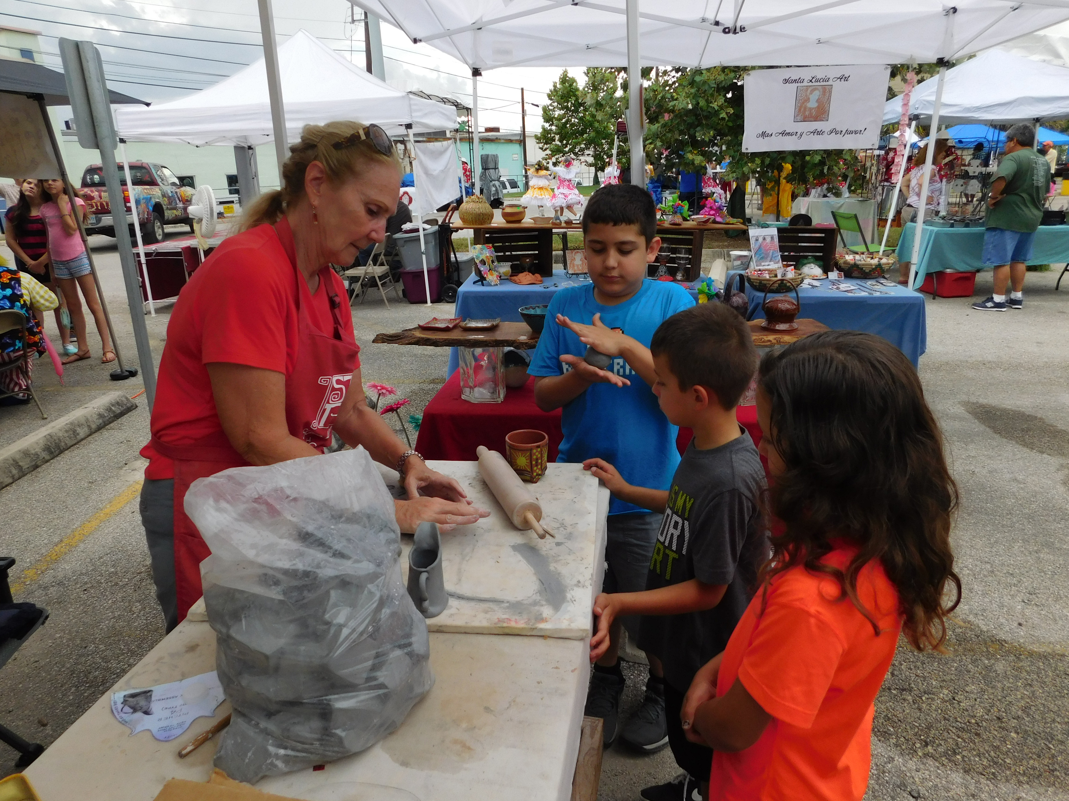 Woman showing three young children how to make pottery in outdoor tent.