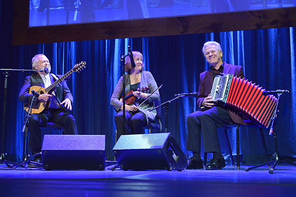A male guitarist, female fiddler, and male accordionist onstage. 