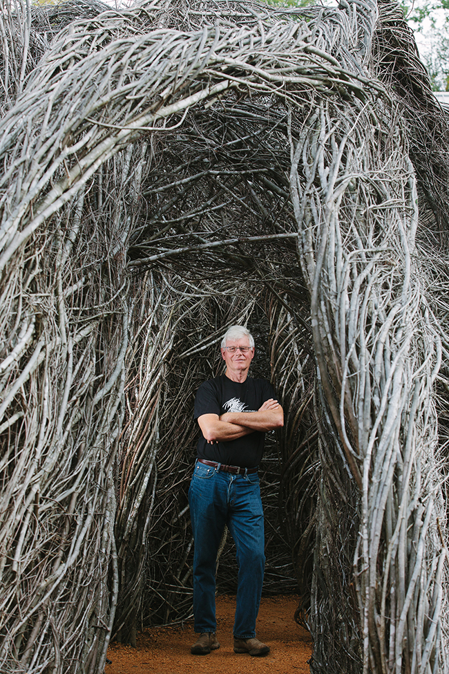 A man standing inside a sculpture made of sticks