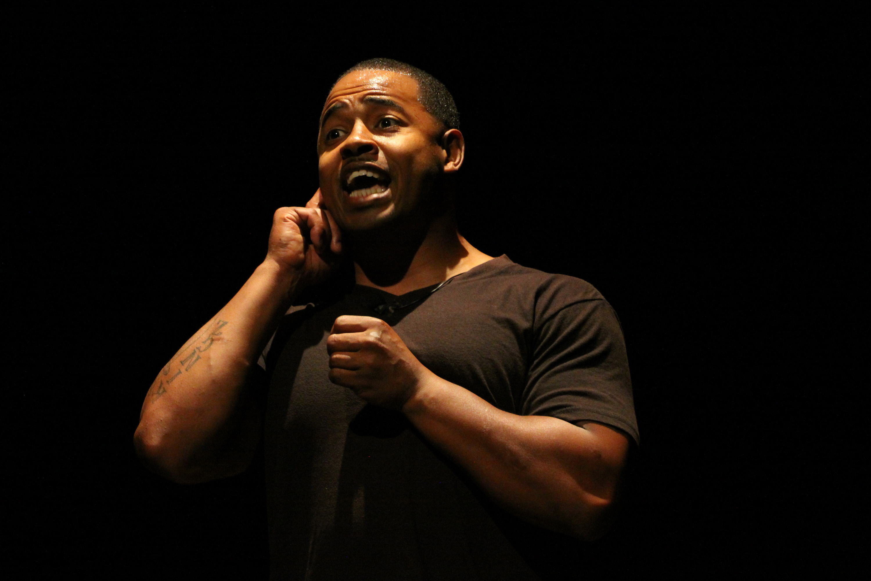 African-American man on stage wearing all black gesticulating. 