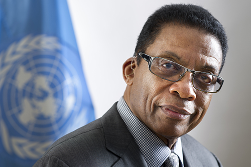 Man wearing glasses in front of a United Nations flag. 