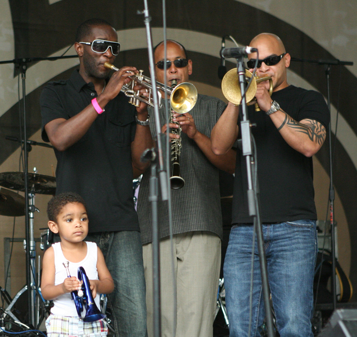 Three men and a boy performing on horns.