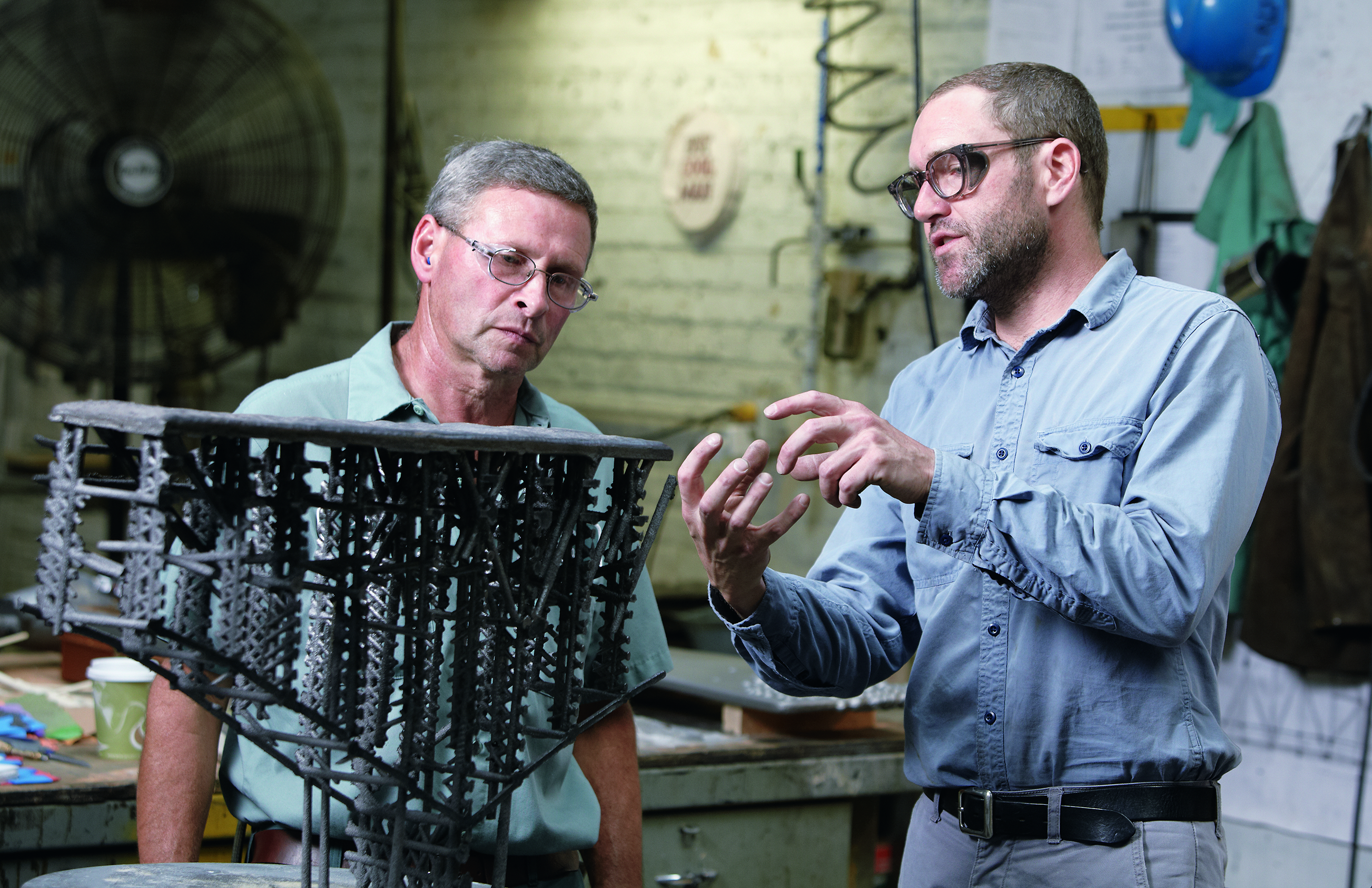 Two men talking in front of machinery. 