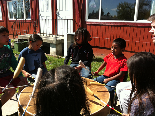 Children in a circle drumming on a large drum. 