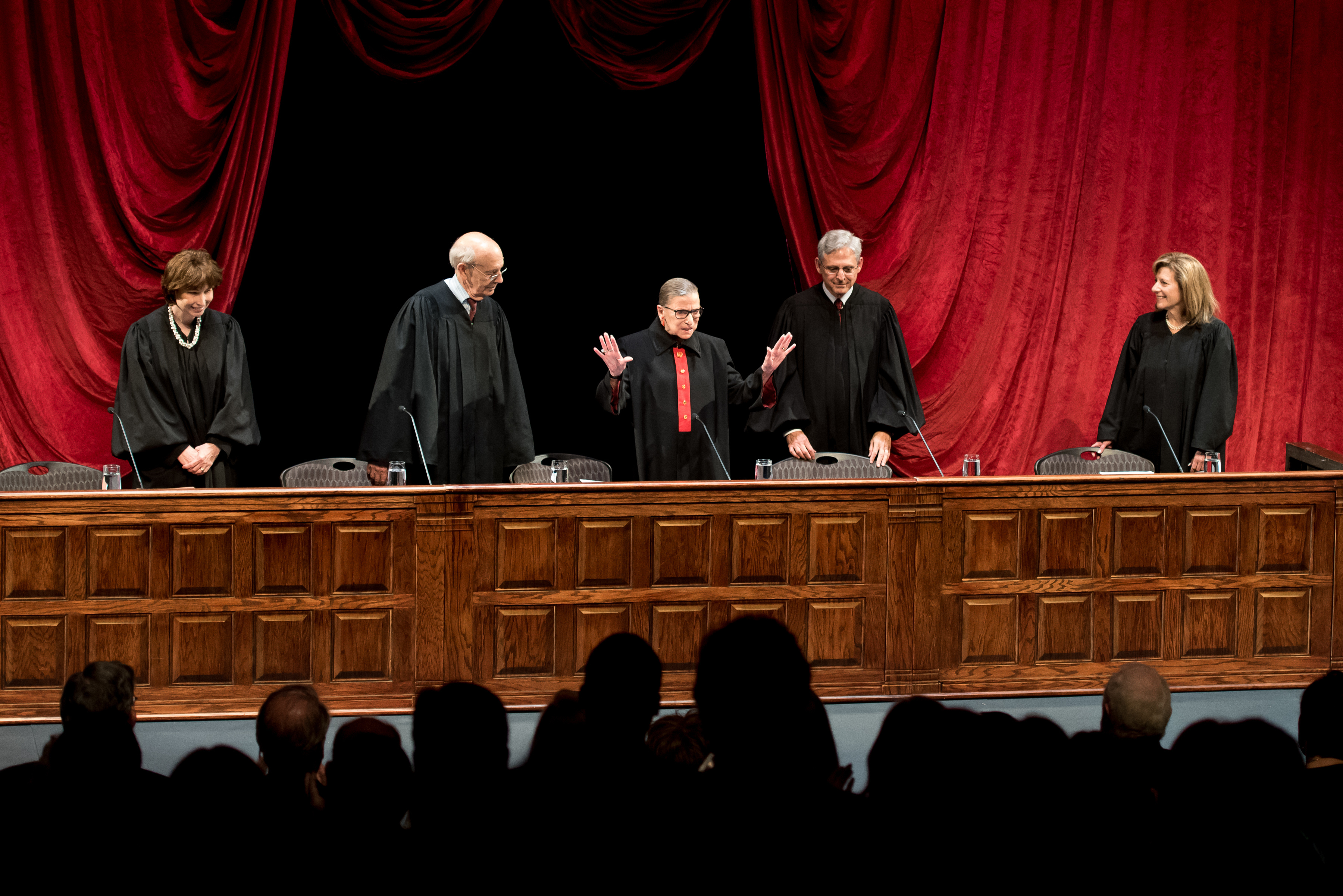 A group of judges standing behind a podium in front of an audience. 