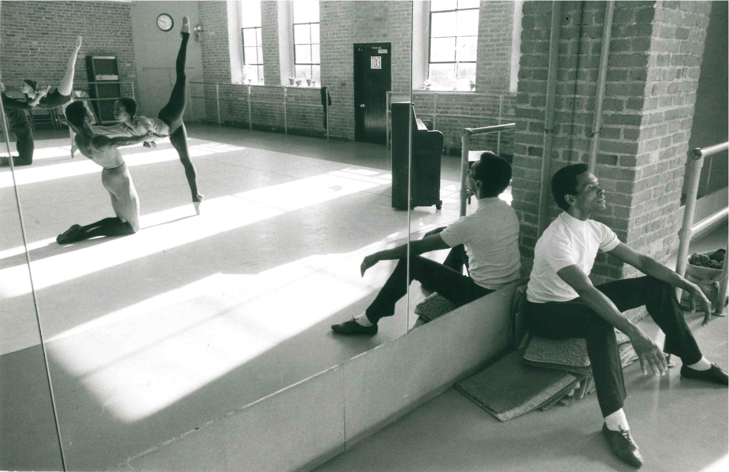 Man sitting against mirror watching two ballet dancers