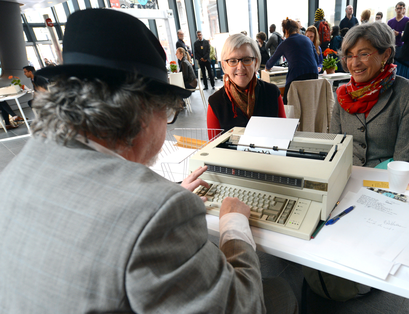 Man in hat typing up poems for two women. 