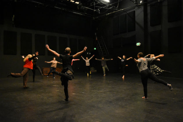 A man and high school students stand in a circle doing arabesques