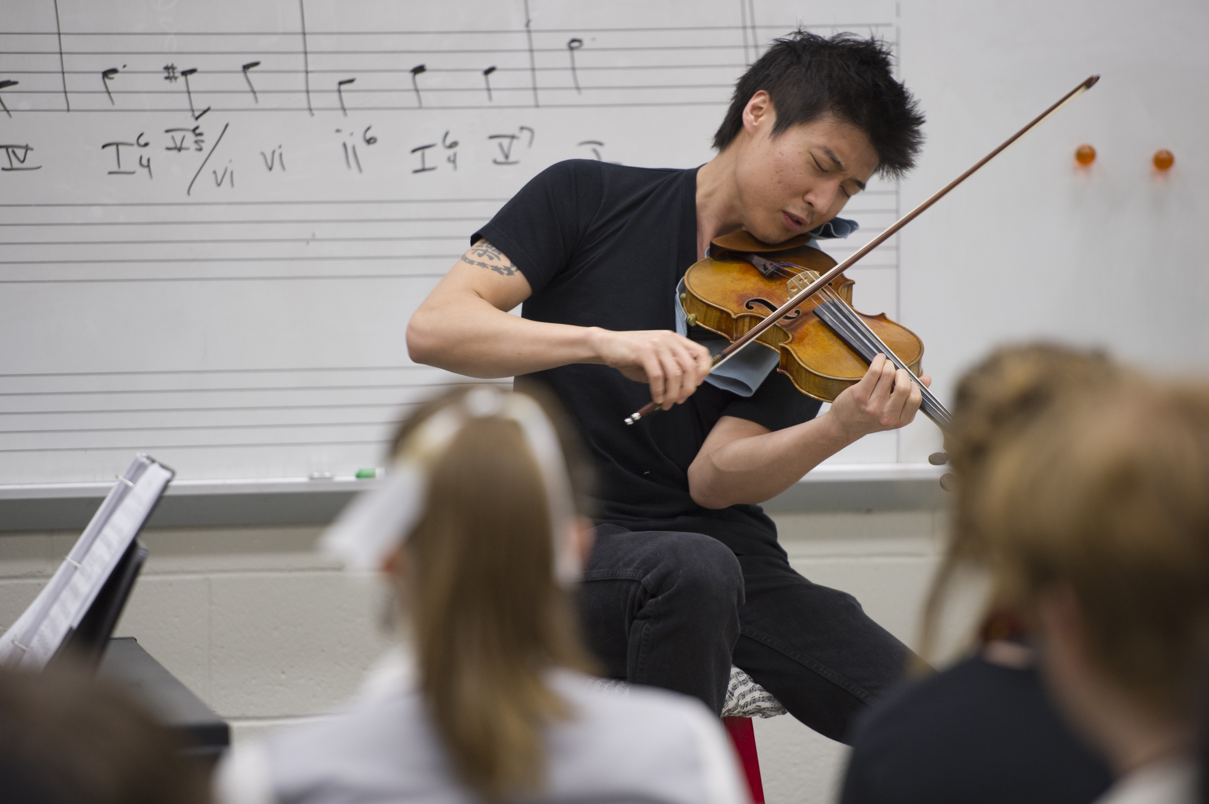 A man performs on the violin in a classroom while students watch.