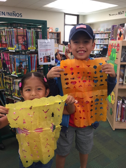 two young kids holding up papel picado panels they have made