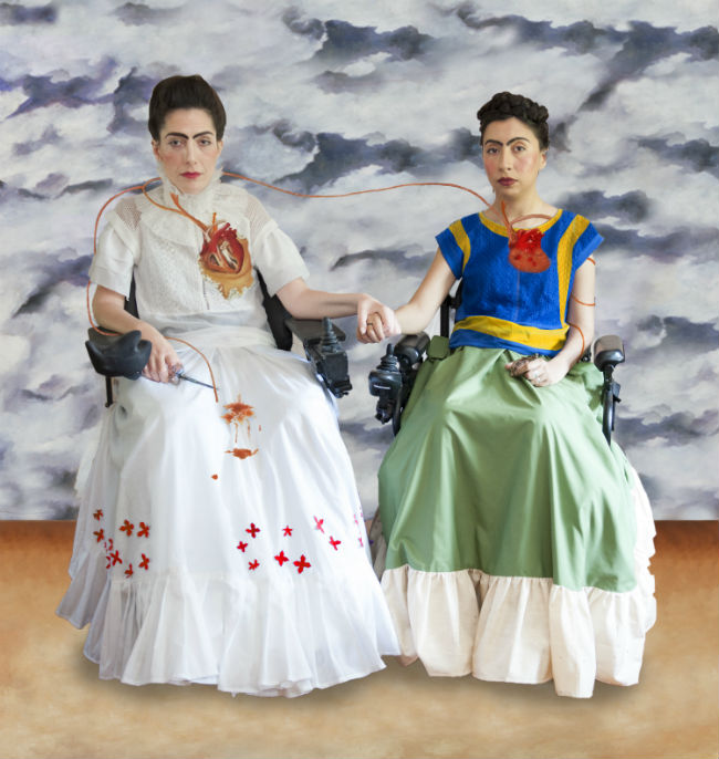 Two women in wheelchairs dressed as Frida Kahlo hold hands
