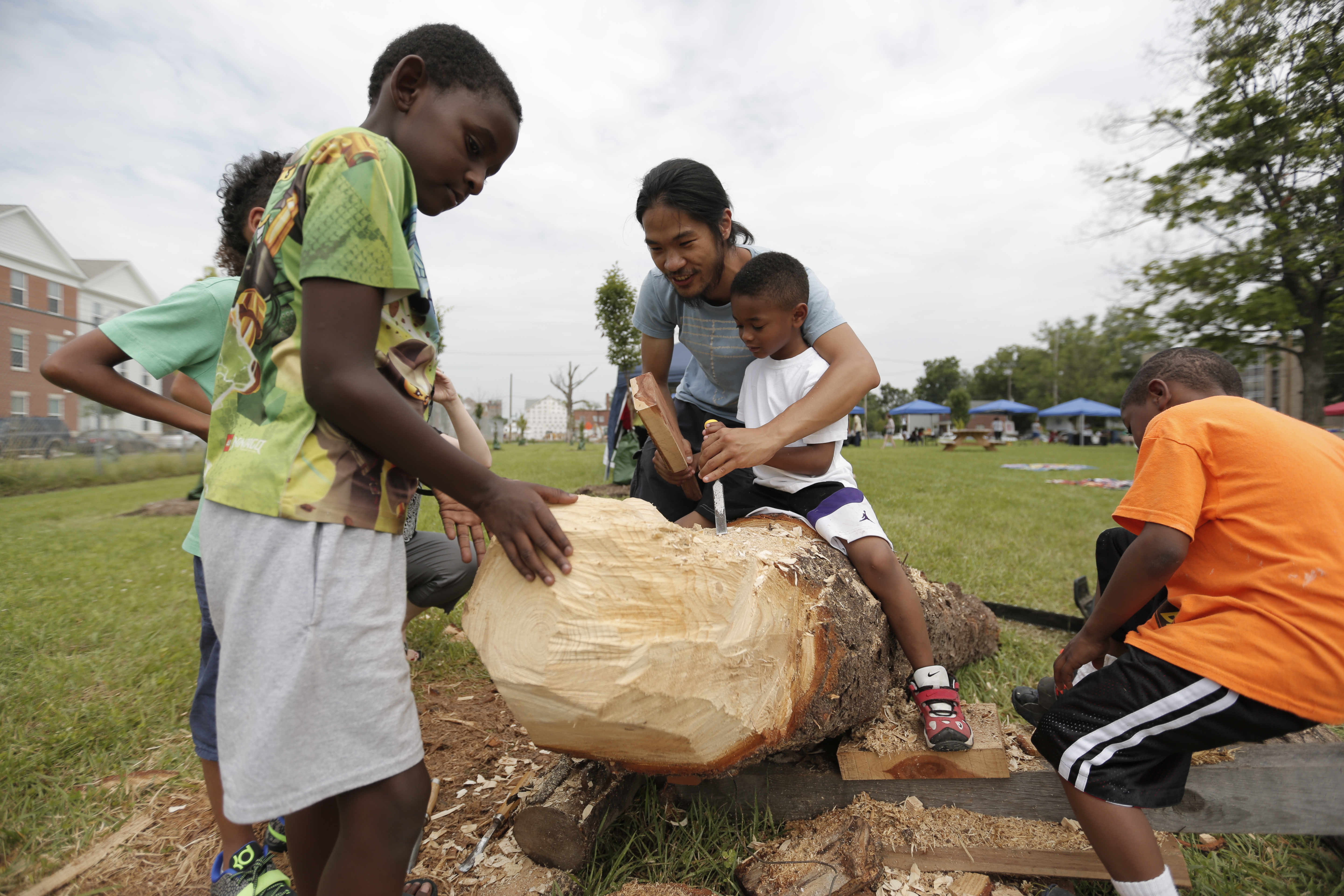 Man and children carving a piece of wood. 